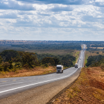 Rodovia de pista dupla em área rural do Centro-Oeste brasileiro com caminhões transportando cargas