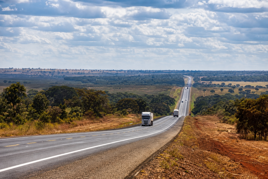 Rodovia de pista dupla em área rural do Centro-Oeste brasileiro com caminhões transportando cargas