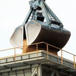 Garra mecânica descarrega carga a granel em um terminal portuário industrial.