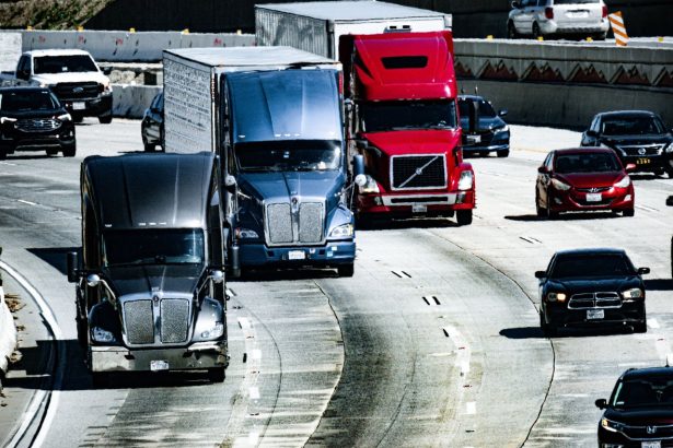 Caminhões e carros trafegam por uma rodovia urbana durante o dia.