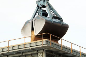 Garra mecânica descarrega carga a granel em um terminal portuário industrial.