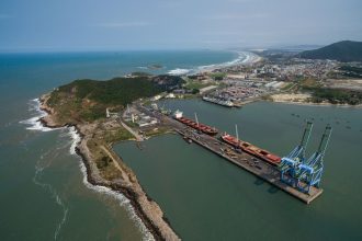 Vista aérea do Porto de Imbituba, com docas, guindastes e embarcações junto à costa brasileira.